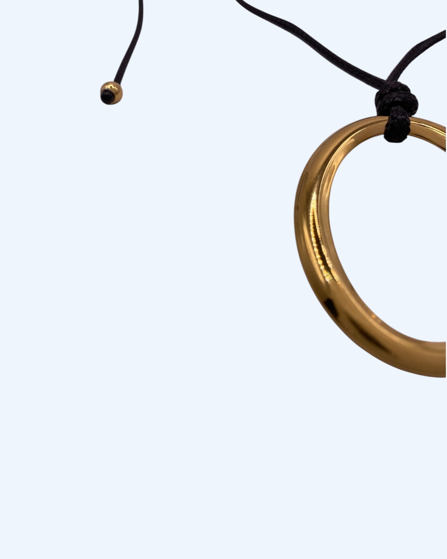 Detalhe do colar com medalhão oval dourado em aço inoxidável e do cordão preto ajustável de colar minimalista feminino. Colar versátil, contemporâneo e minimalista.