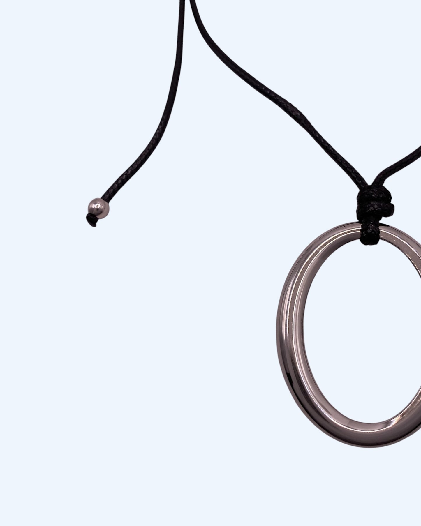 Detalhe do colar com medalhão oval prateado em aço inoxidável e do cordão preto ajustável de colar minimalista feminino. Colar versátil, contemporâneo e minimalista.