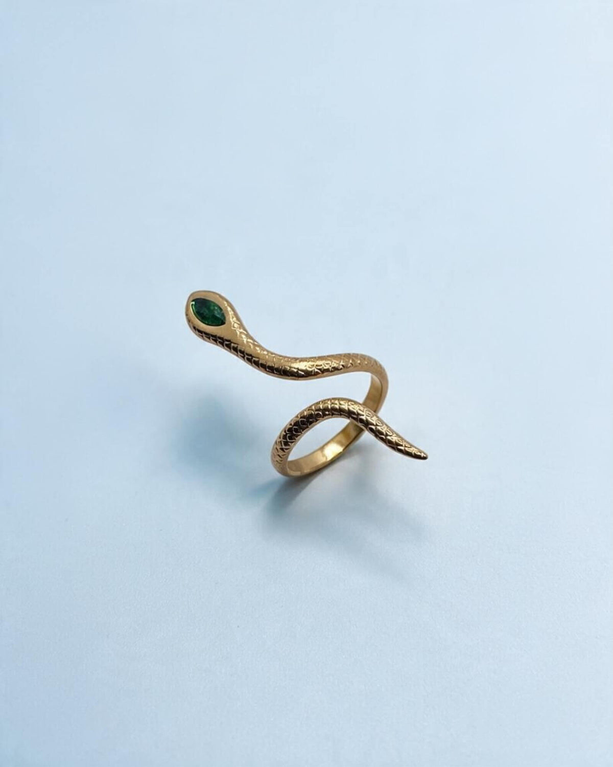 Anel serpente Víbora dourado visto de cima em ângulo, com aro aberto, textura de escamas e detalhe verde na cabeça.