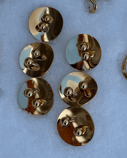 Vista frontal dos Brincos longos dourados em aço inoxidável, com discos unidos por piercings. 