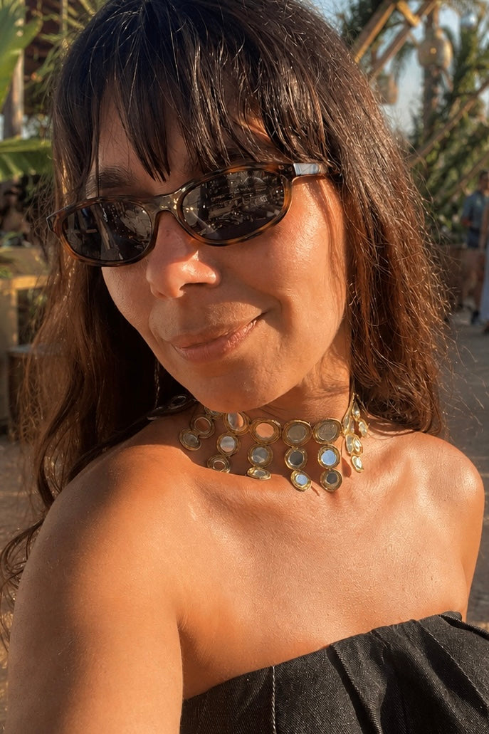 Detalhe de modelo a usar o Vista frontal do choker dourado em faixa de tecido com espelhos redondos HALO. Colar ideal para festas e cerimónias.