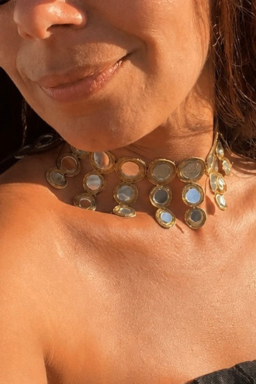 Detalhe de modelo a usar o Vista frontal do choker dourado em faixa de tecido com espelhos redondos HALO. Colar ideal para festas e cerimónias.