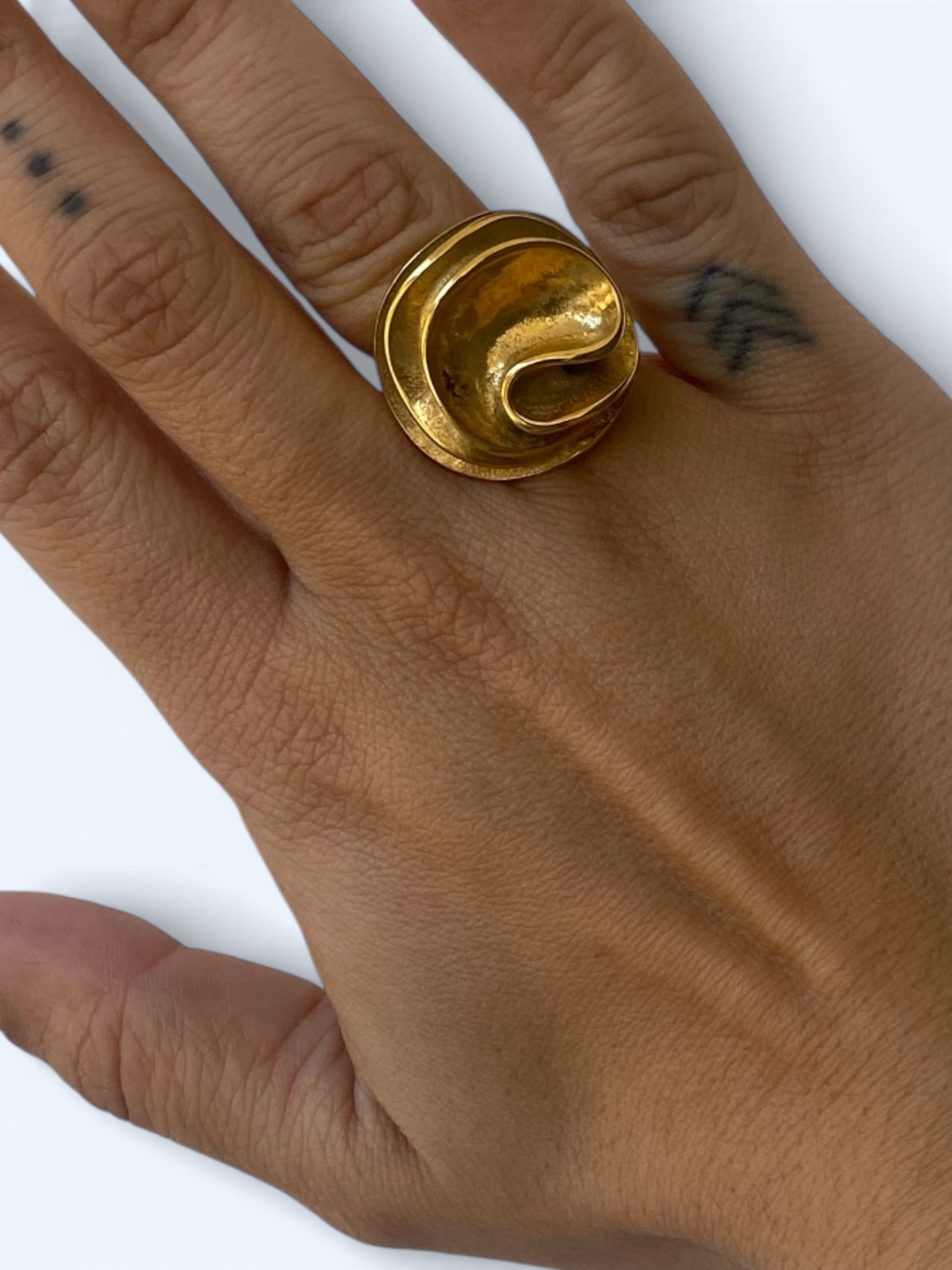 Vista a ser usado na mão pela modelo do Anel chunky grande com ondas orgânicas em aço inoxidável dourado.
