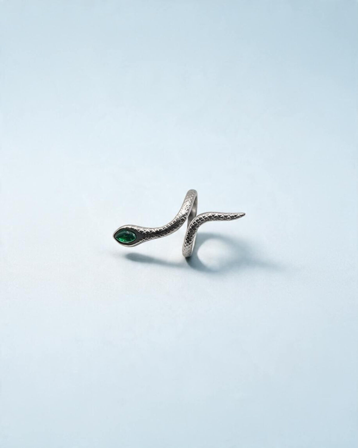 Anel cobra prateado visto de lado, com corpo curvo, textura de escamas e detalhe verde na cabeça.