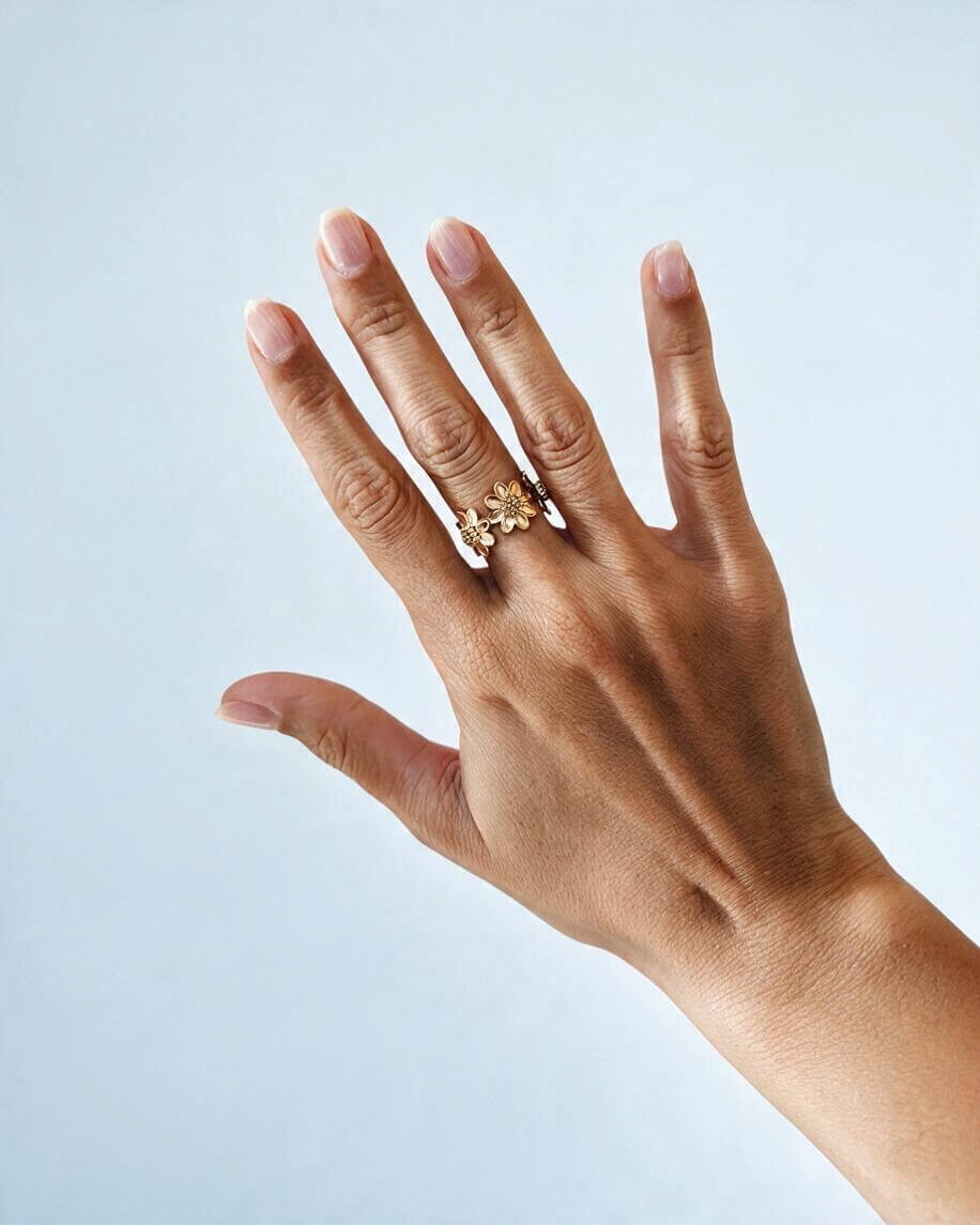 Anel dourado de flores usado na mão aberta, mostrando a proporção e o efeito do desenho floral no dedo.