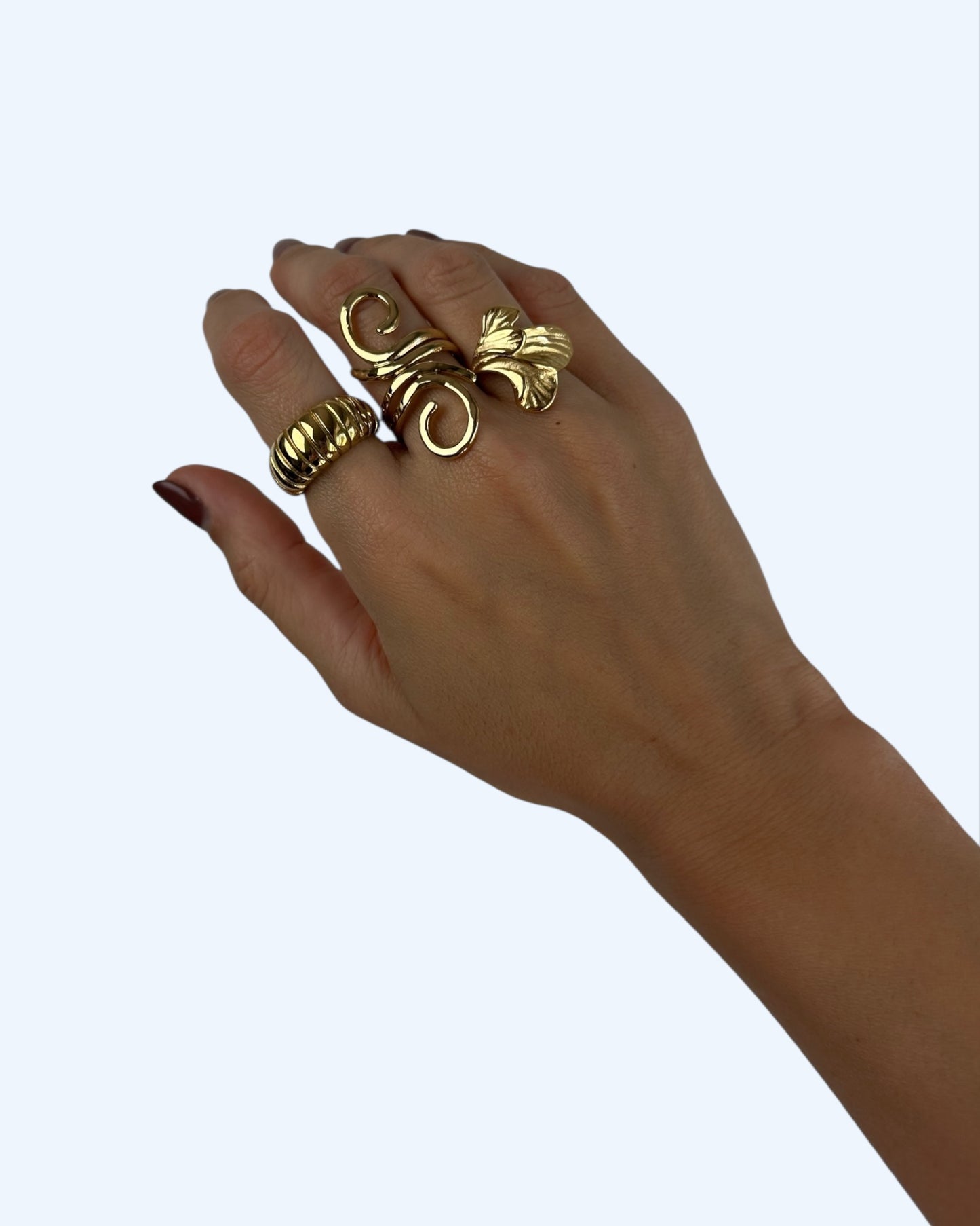 Vista do anel dourado longo com curvas em aço inoxidável a ser usado no dedo, em conjunto com outros dois anéis.