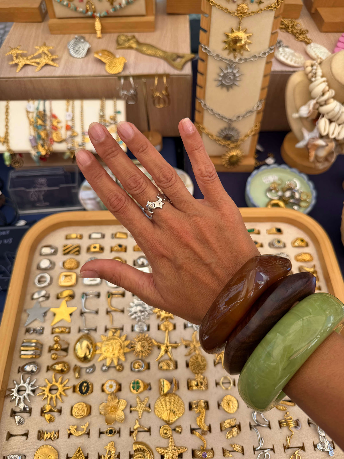 Anel de estrelas prateado usado na mão, com os dedos estendidos e pulseiras no pulso.