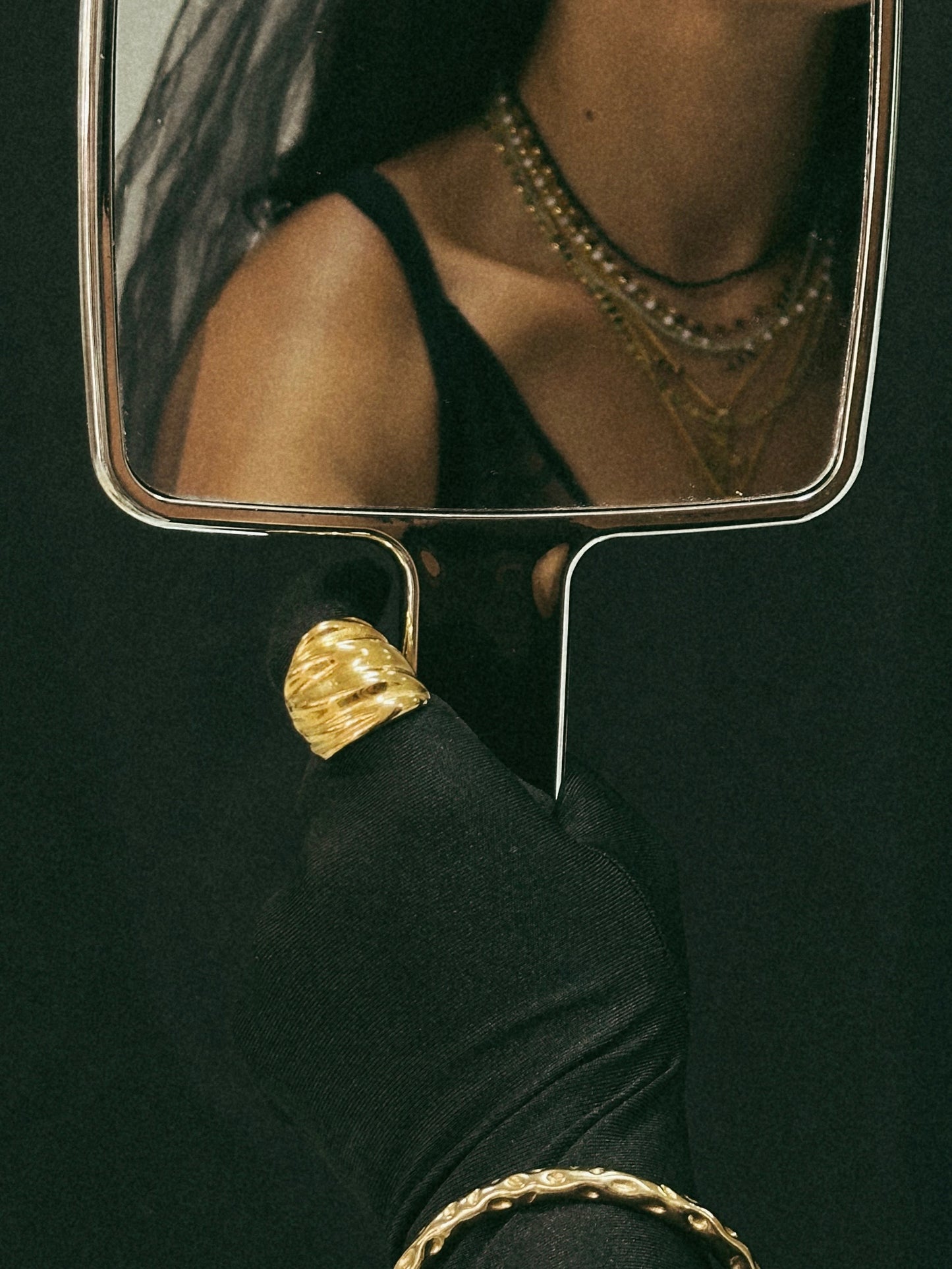 Anel maxi dourado em aço inoxidável com uma textura ondulada e volume elegante. Vista a ser usado no dedo.