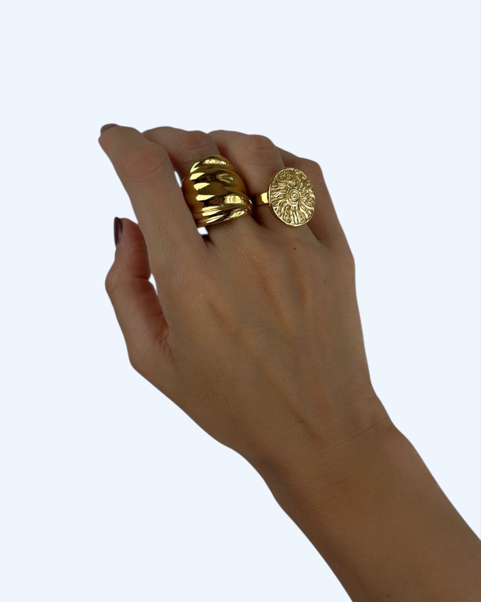 Anel maxi dourado em aço inoxidável com uma textura ondulada e volume elegante. Vista a ser usado com outro anel.