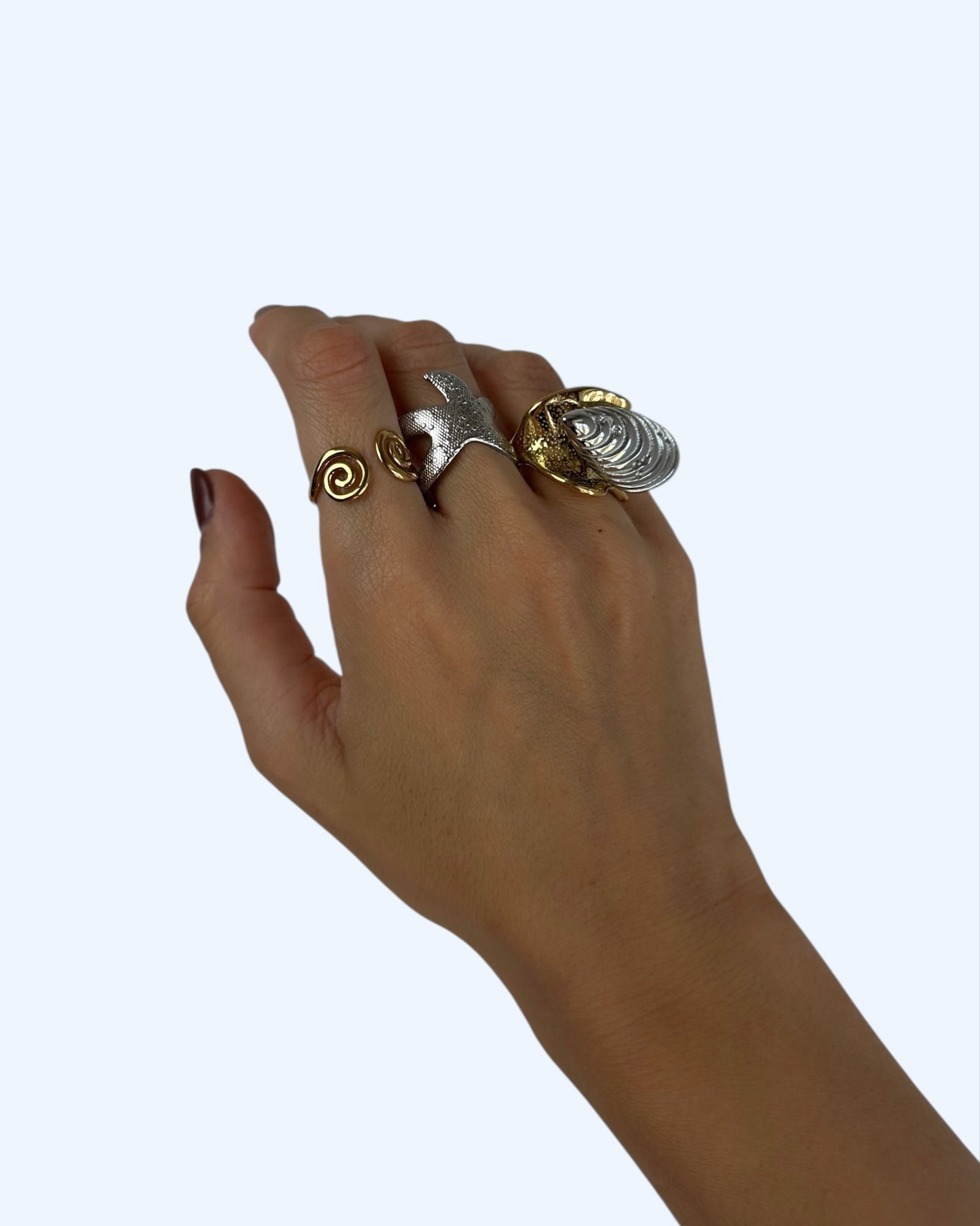 Vista a ser usado na mão, do anel metalizado com concha em aço inoxidável. É um anel bold e texturizado dourado com uma concha prateada no topo.