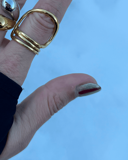 Vista a ser usado no dedo do anel minimalista que contorna o dedo dourado em aço inoxidável.
Tem um design geométrico versátil que permite ser usado em diferentes posições. É simultaneamente clean e bold.