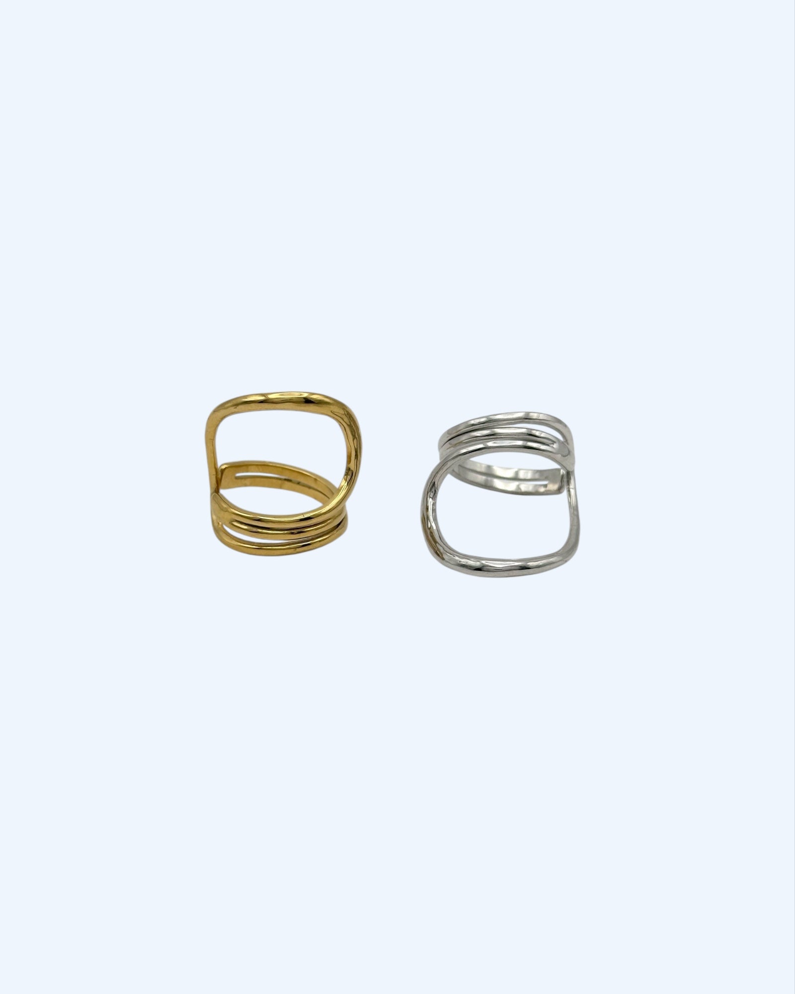 Vista frontal do anel minimalista que contorna o dedo dourado em aço inoxidável e do anel minimalista que contorna o dedo prateado em aço inoxidável. São simultaneamente clean e bold.