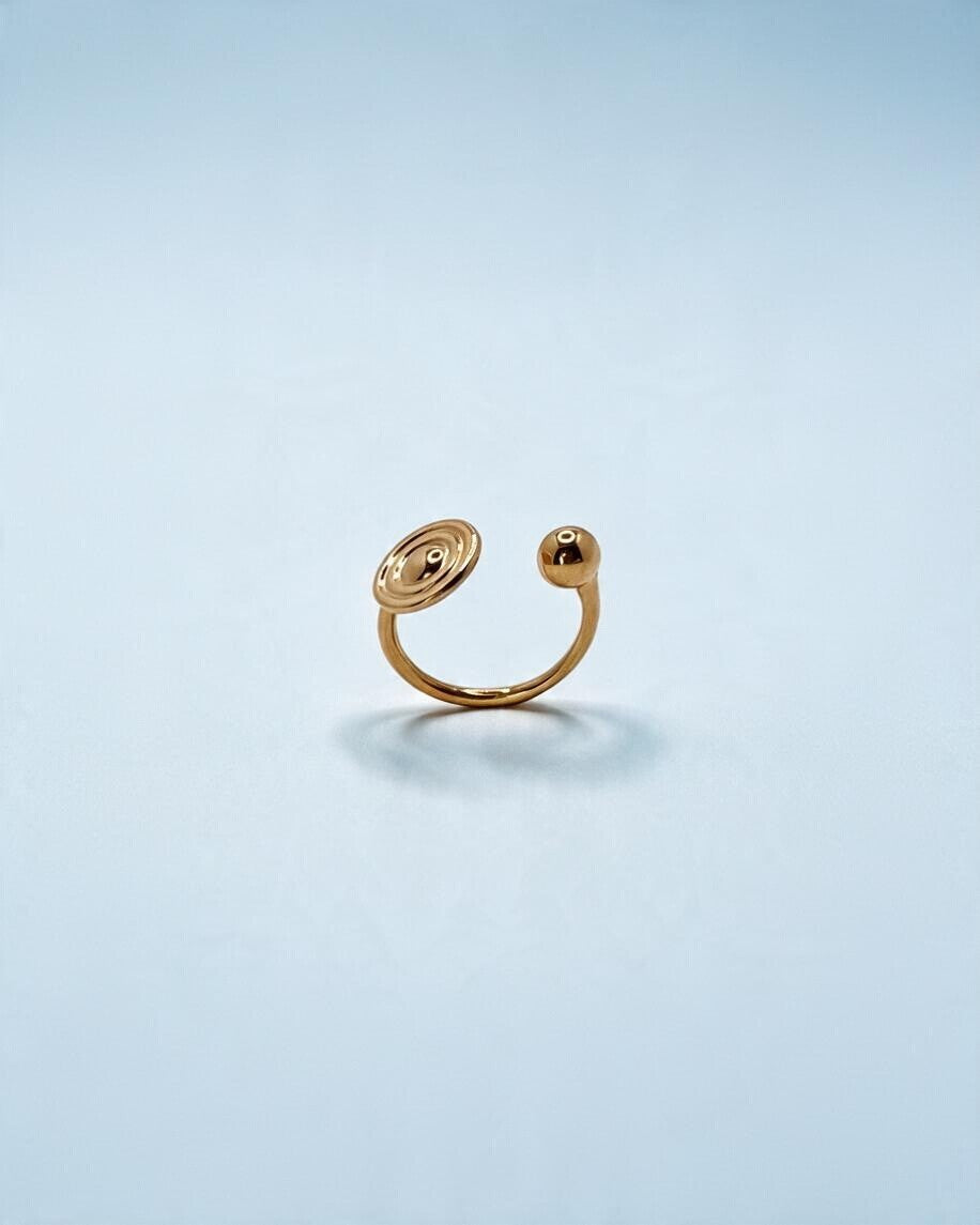 Anel Órbita dourado em aço inoxidável, em pé, mostrando o aro aberto ajustável, o disco e a esfera.