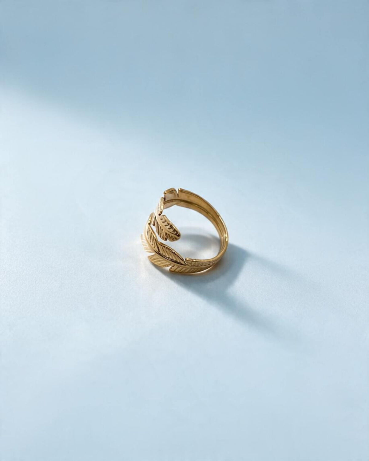 Anel Pluma dourado ajustável em aço inoxidável visto de lado, mostrando o interior do aro e as pontas em forma de pena.