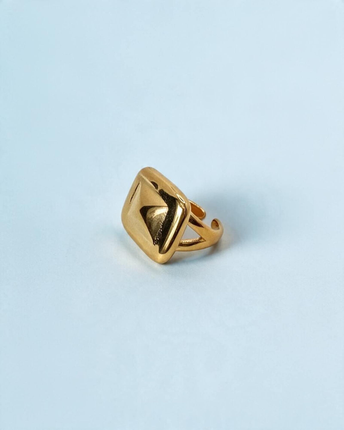 Anel Prisma dourado em aço inoxidável, visto a três quartos, com frente quadrada e relevo em pirâmide.