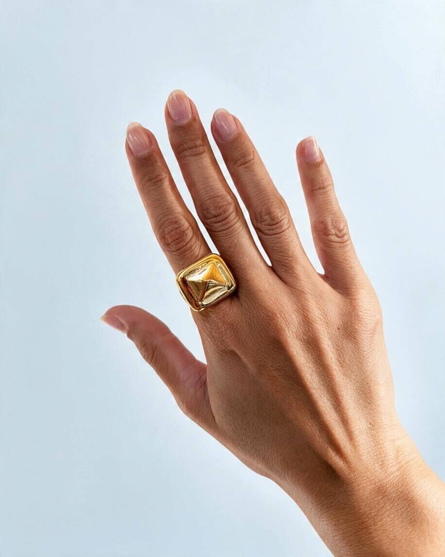 Anel quadrado Prisma dourado usado no indicador, com a mão aberta, mostrando o tamanho da peça em relação aos dedos.
