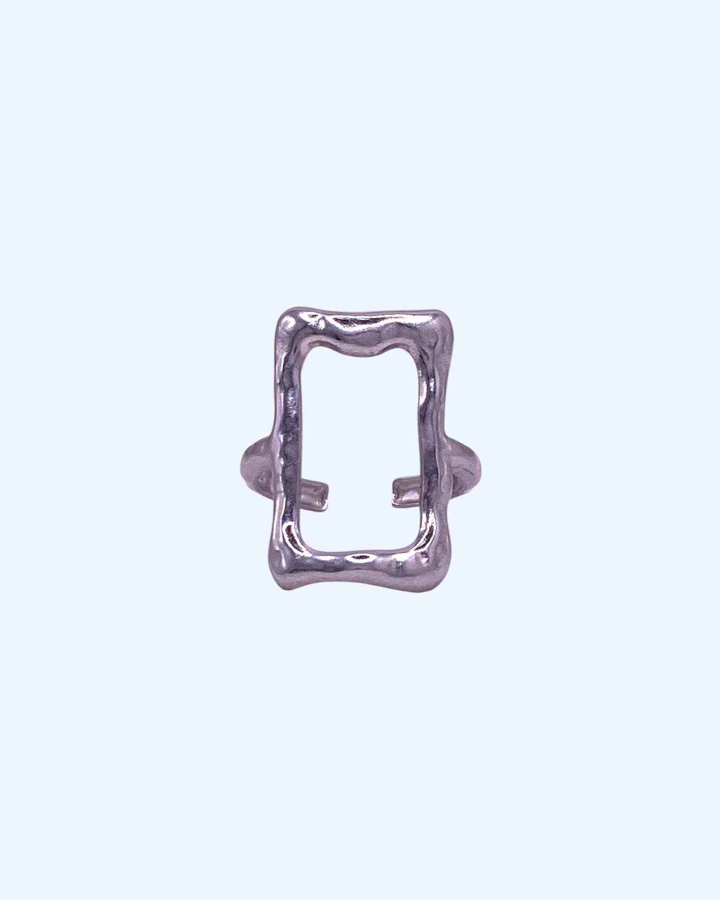 Vista frontal do Anel prateado ajustável em aço inoxidável de forma retangular irregular. Este anel tem linhas orgânicas e livres, em formato retagular aberto de frame é de design contemporâneo, é um anel minimalista leve, idela como bijuteria minimalista, anel contemporâneo, para looks casuais e de quem gosta de bijuteria artistica mas moderna.