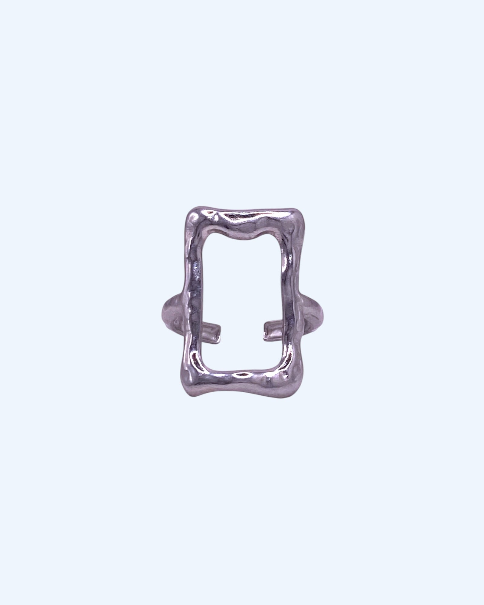 Vista frontal do Anel prateado ajustável em aço inoxidável de forma retangular irregular. Este anel tem linhas orgânicas e livres, em formato retagular aberto de frame é de design contemporâneo, é um anel minimalista leve, idela como bijuteria minimalista, anel contemporâneo, para looks casuais e de quem gosta de bijuteria artistica mas moderna.