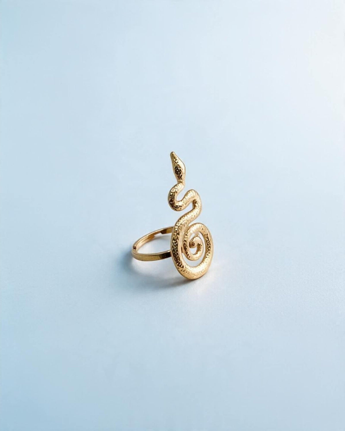 Anel serpente dourado visto a três quartos, com corpo texturado, cauda em espiral e aro visível à esquerda.