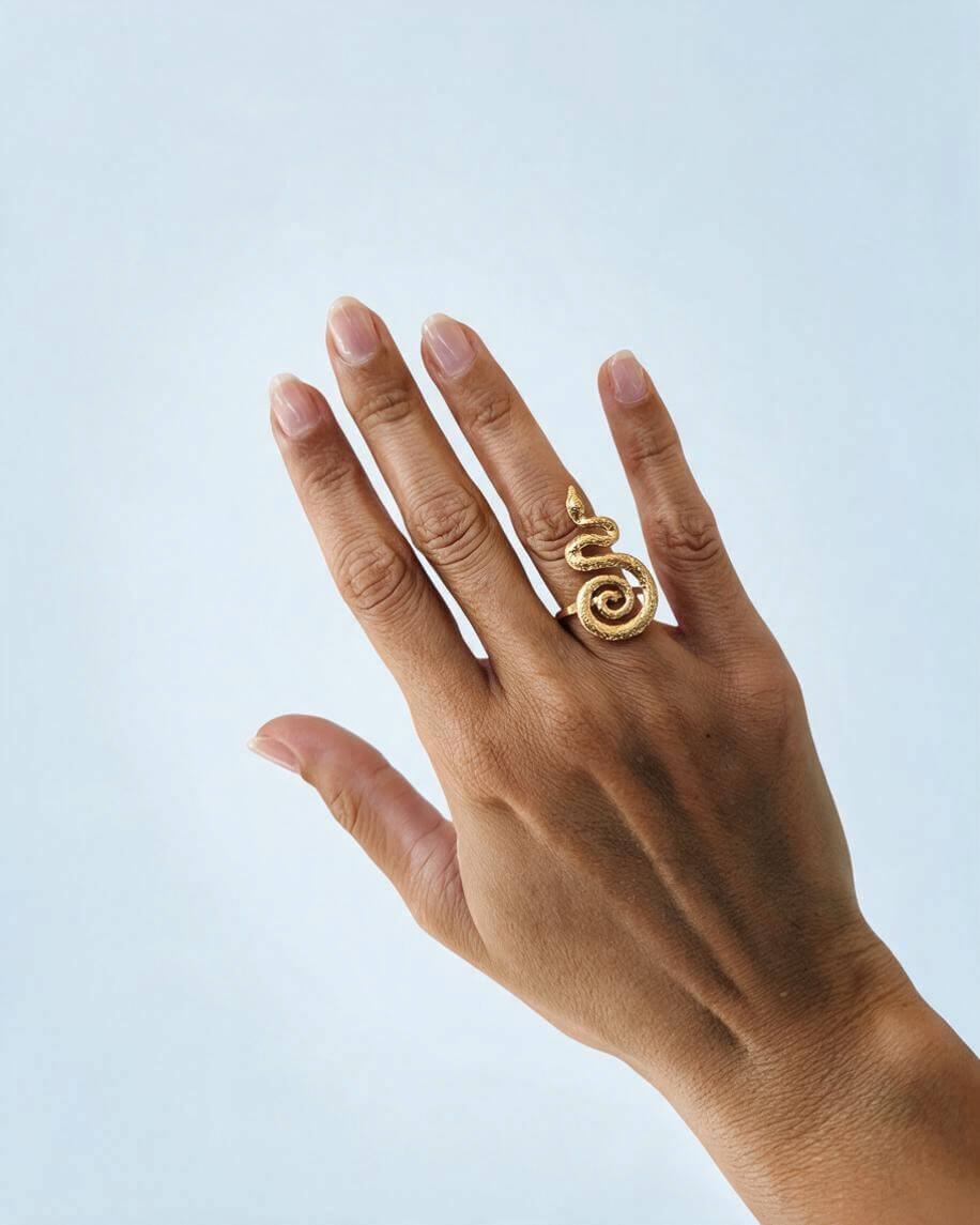 Anel serpente dourado no dedo anelar de uma mão aberta, mostrando o tamanho do desenho e a cauda em espiral.
