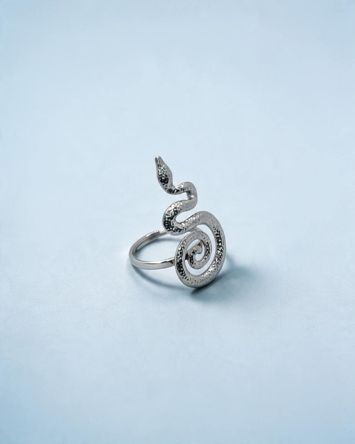 Anel serpente prateado visto a três quartos, com corpo texturado, cauda em espiral e aro visível à esquerda.