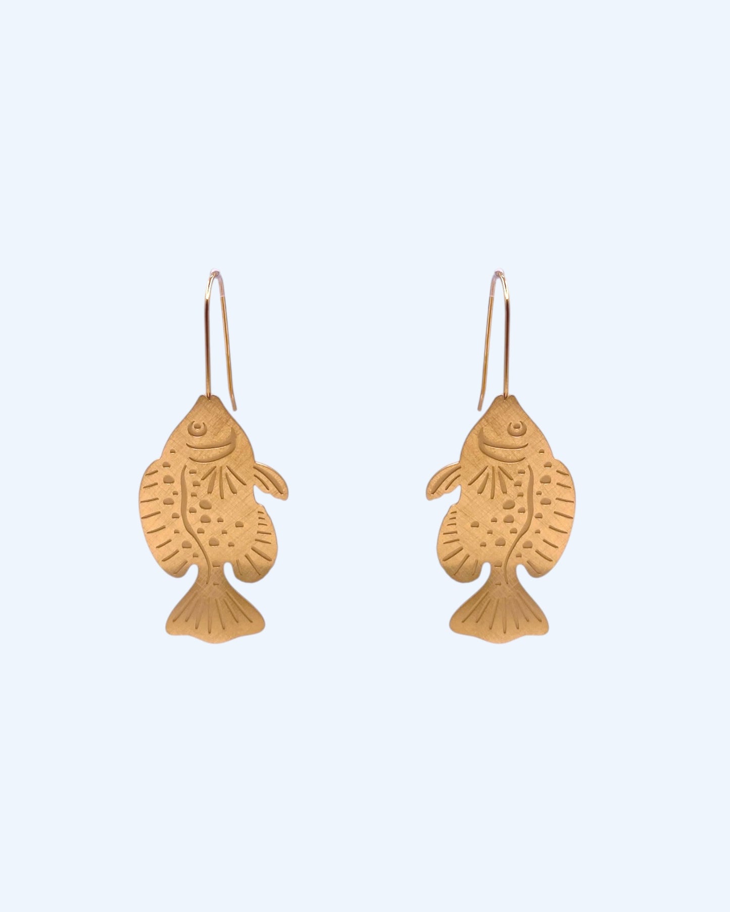 Vista frontal dos Brincos dourados boho em forma de um peixe exótico em aço inoxidável. Estes brincos em forma de peixe são bijuteria de verão, um acessório trendy para it girls e looks casuais, de verão e de praia.