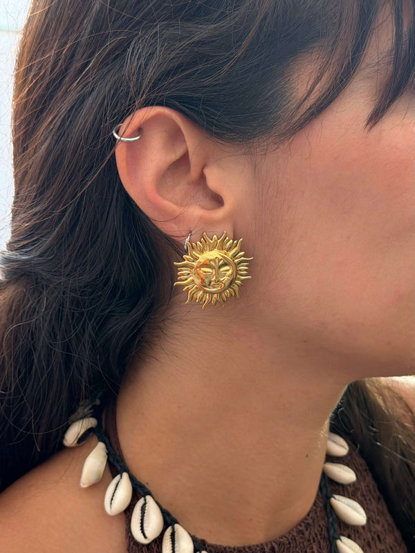 Vista na modelo dos brincos dourados de design místico celestial, em forma do desenho do sol com a lua. Este brincos são perfeitos para o verão e tanto para usar o dia a dia, casualmente, como em looks boho, em sunsets e festas e festivais de verão.