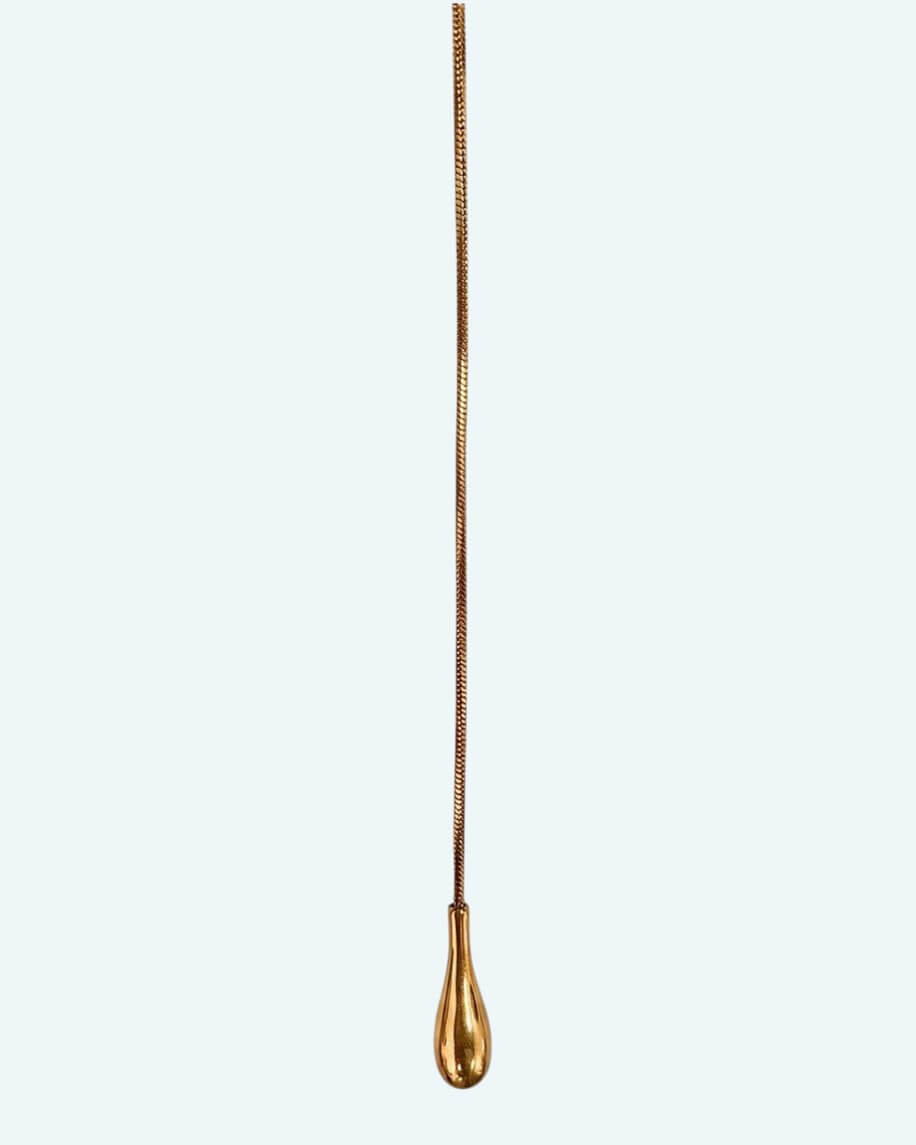 Vista detalhe do pendente do colar Flow que é um cordão metálico dourado ajustável em aço inoxidável, com um design em Y que cria uma linha fluida escultural.
Contorna o pescoço, passa pela peça central e termina num pendente em forma de gota. É possível usa-lo junto ao pescoço como choker com o cordão pendurado mais comprido, ou deixa-lo mais solto para uma vibe descontraída.
Um colar para quebrar a simplicidade de uma gola redonda, para intensificar um decote em V ou contrariar um top de ombro a ombro.