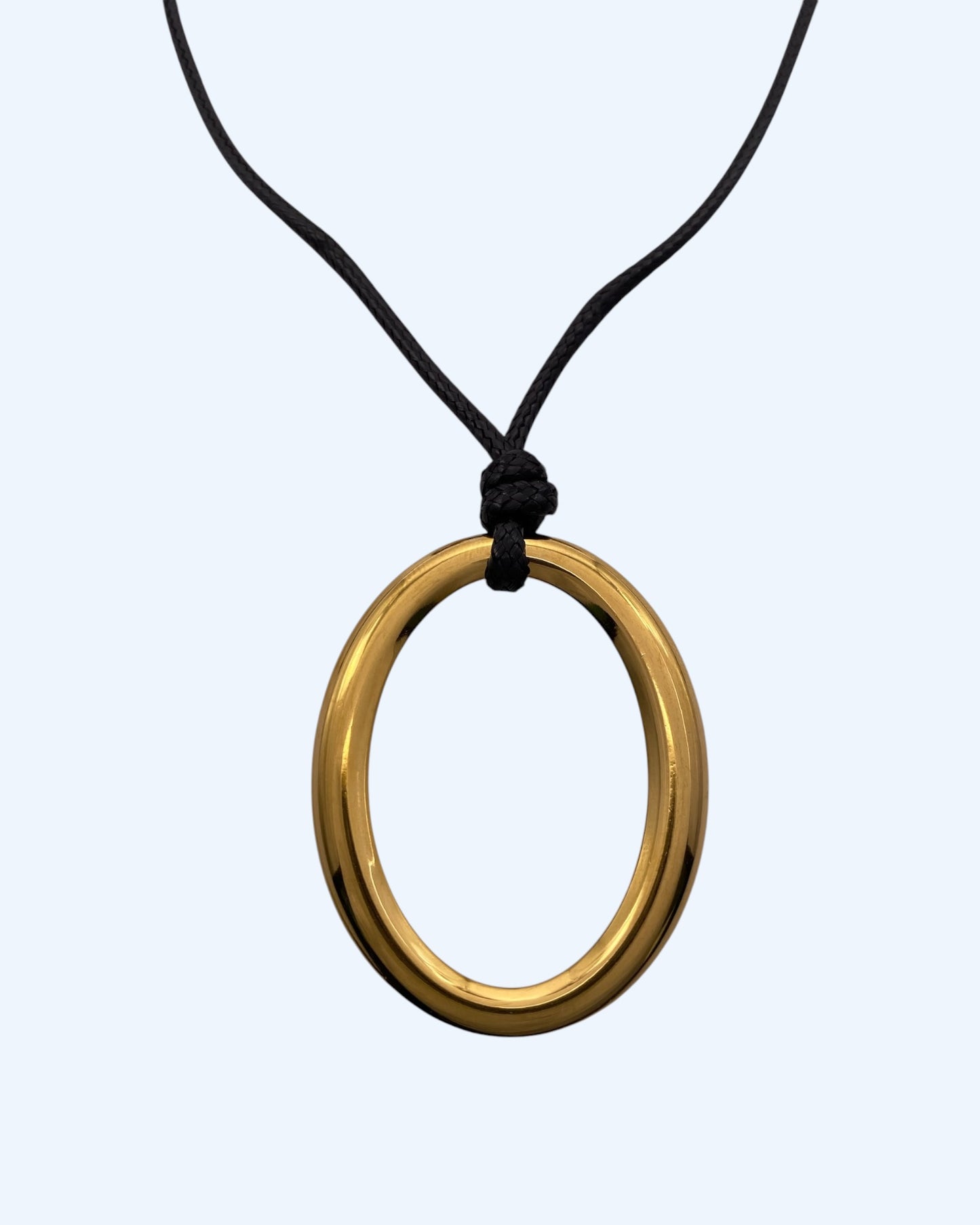 Detalhe do medalhão oval dourado em aço inoxidável e do cordão preto ajustável de colar minimalista feminino.  Colar versátil, contemporâneo e minimalista.