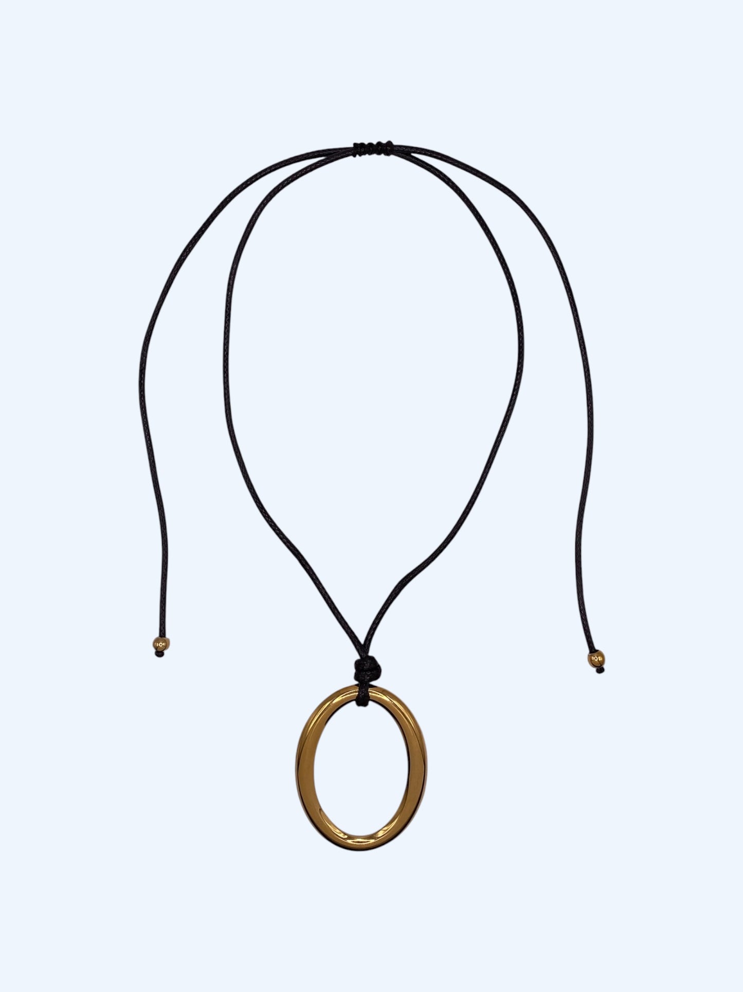 Colar ajustável em choker com medalhão oval dourado em aço inoxidável e cordão preto. Colar versátil, contemporâneo e minimalista.