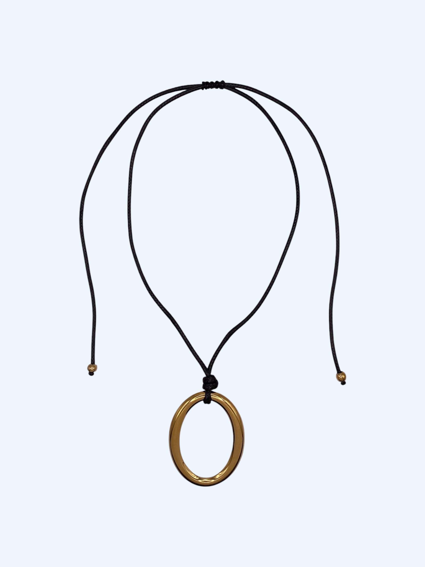 Colar ajustável em choker com medalhão oval dourado em aço inoxidável e cordão preto. Colar versátil, contemporâneo e minimalista.