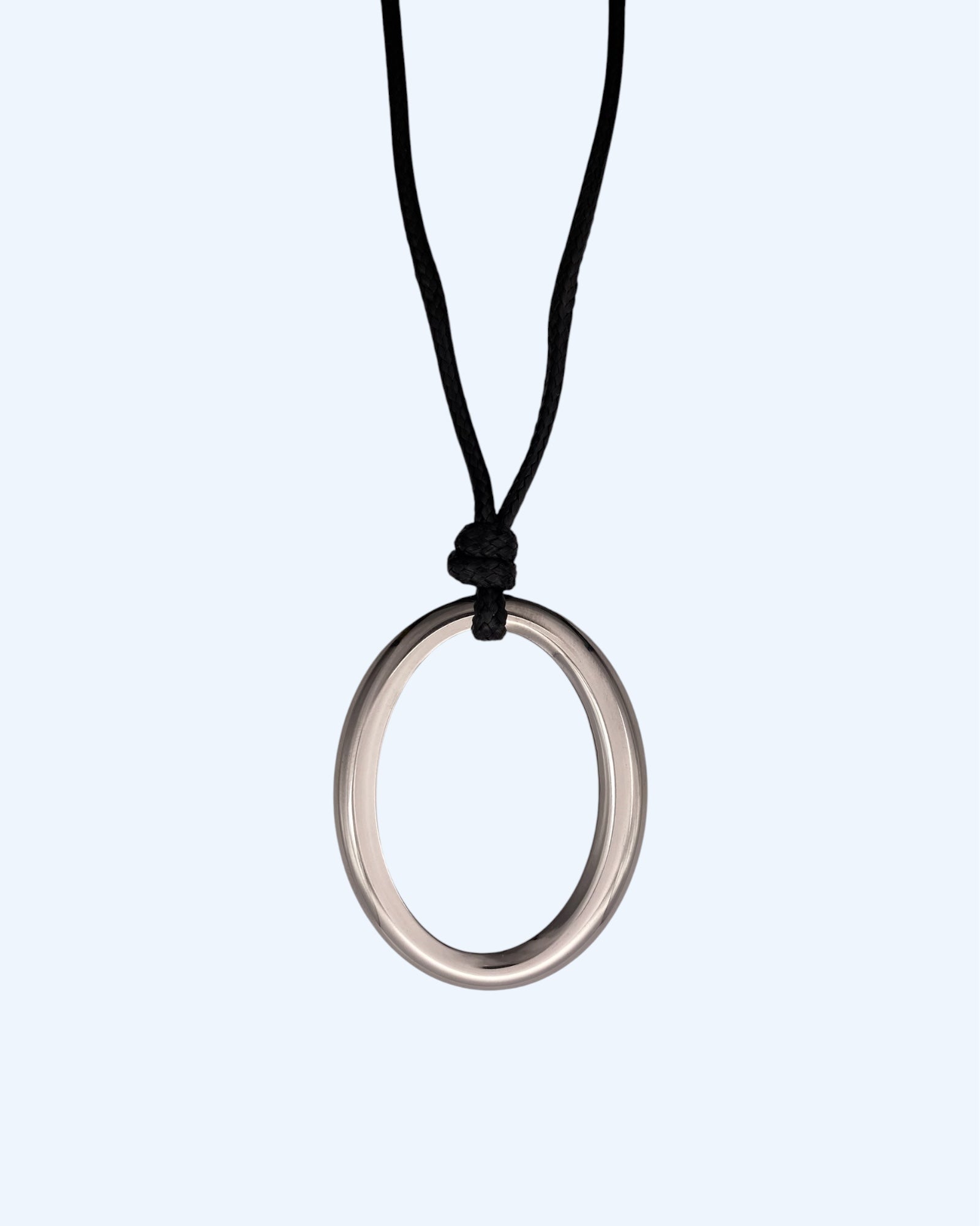 Detalhe do medalhão oval prateado em aço inoxidável e do cordão preto ajustável de colar minimalista feminino.  Colar versátil, contemporâneo e minimalista.