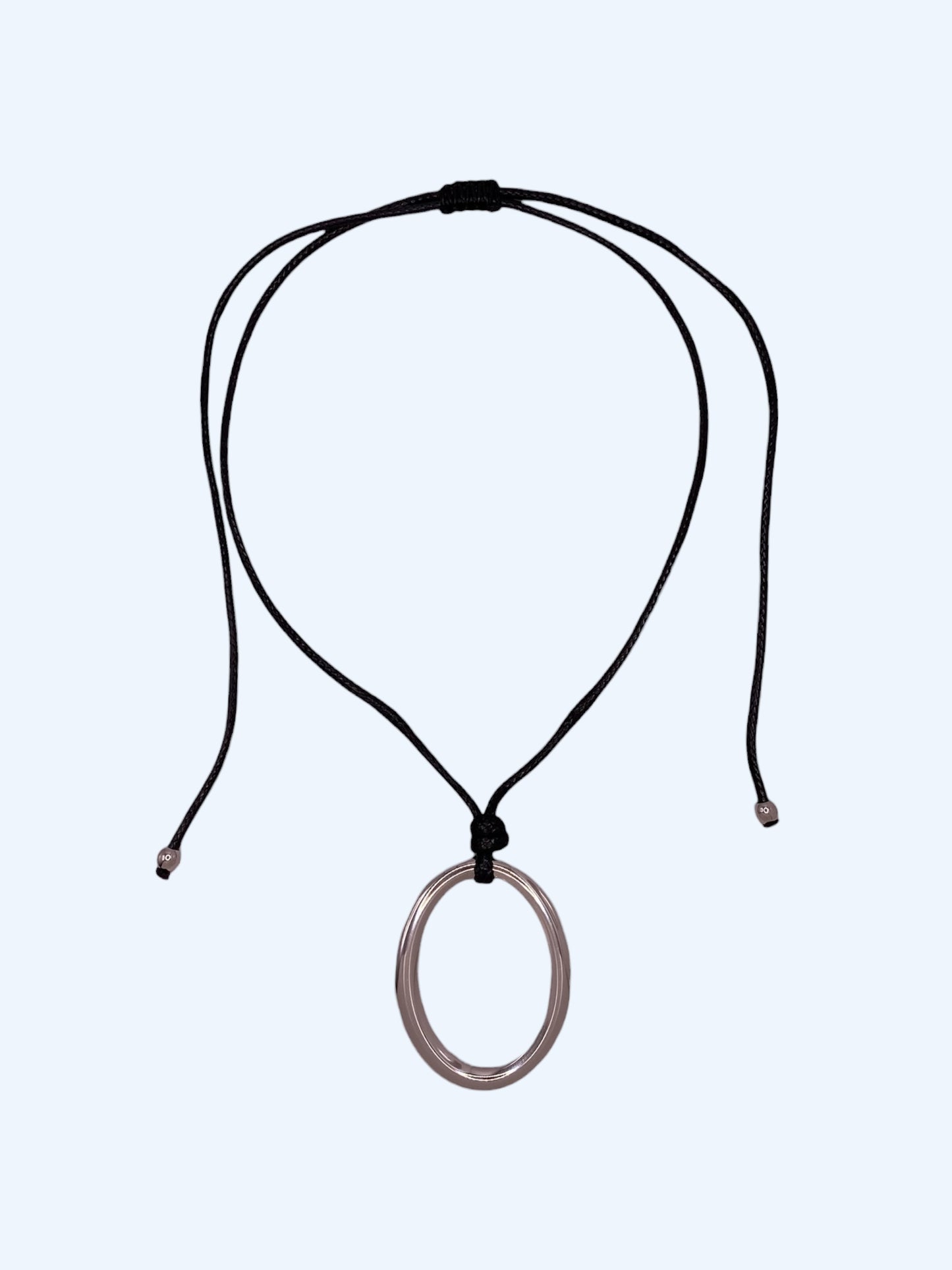 Colar ajustável em choker com medalhão oval prateado em aço inoxidável e cordão preto. Colar versátil, contemporâneo e minimalista.