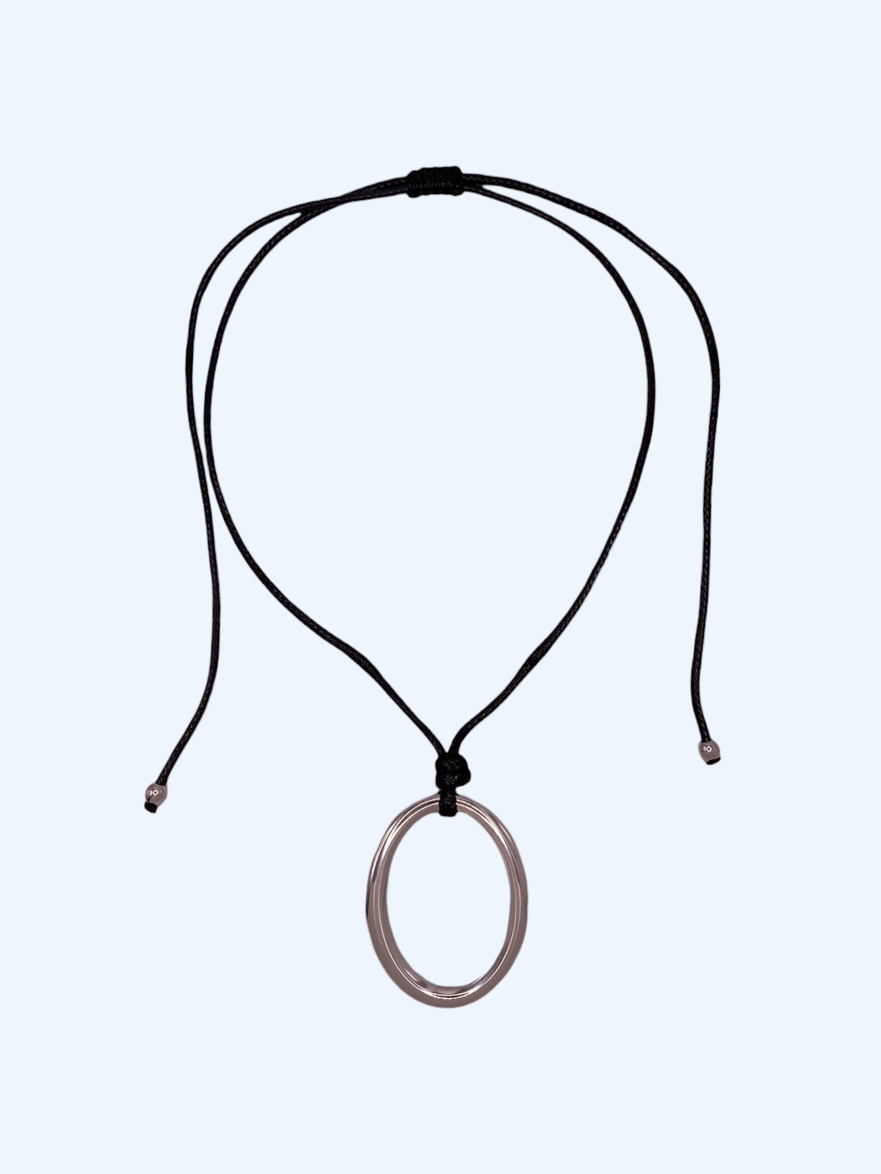 Colar ajustável em choker com medalhão oval prateado em aço inoxidável e cordão preto. Colar versátil, contemporâneo e minimalista.