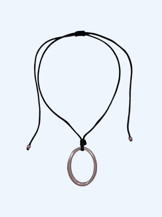 Colar ajustável em choker com medalhão oval prateado em aço inoxidável e cordão preto. Colar versátil, contemporâneo e minimalista.