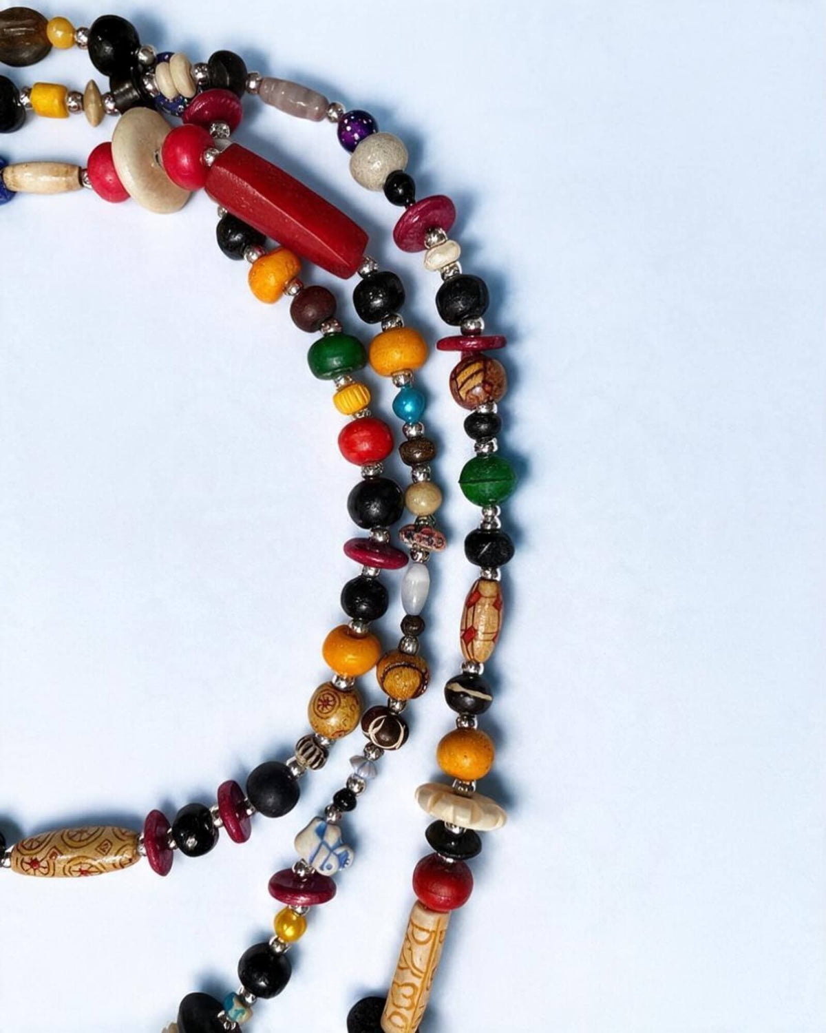 Pormenor do colar multicolor com contas redondas, discos e uma conta vermelha alongada, entre pequenos separadores metalizados.