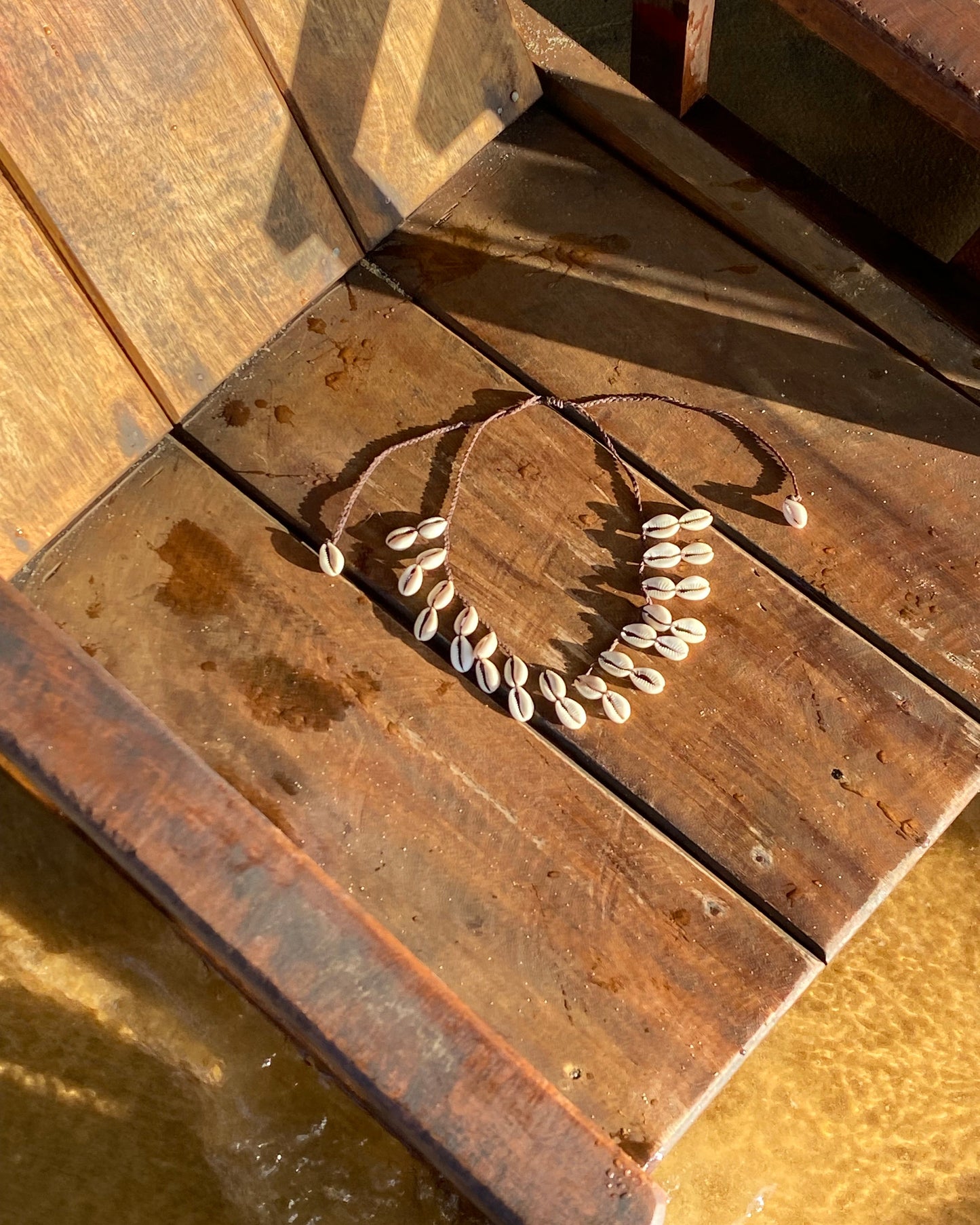 Detalhe do Colar com búzios cauri naturais em cordão entrançado castanho ajustável. Este colar surfer é um colar de búzios para usar em festas, festivais e dias de verão. Colar boho casual que ajusta como gargantilha de búzios ou colar comprido de búzios.