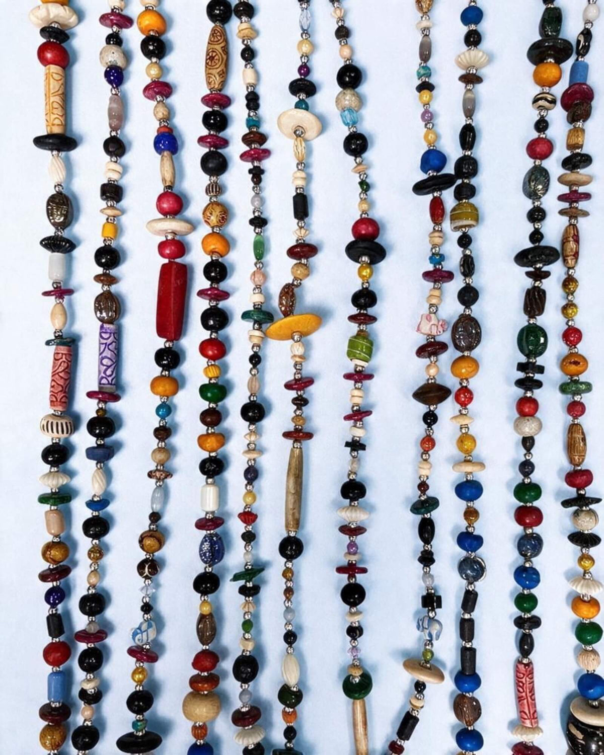 Vários colares de contas multicolor alinhados lado a lado, mostrando diferentes combinações de cores, formas e padrões.