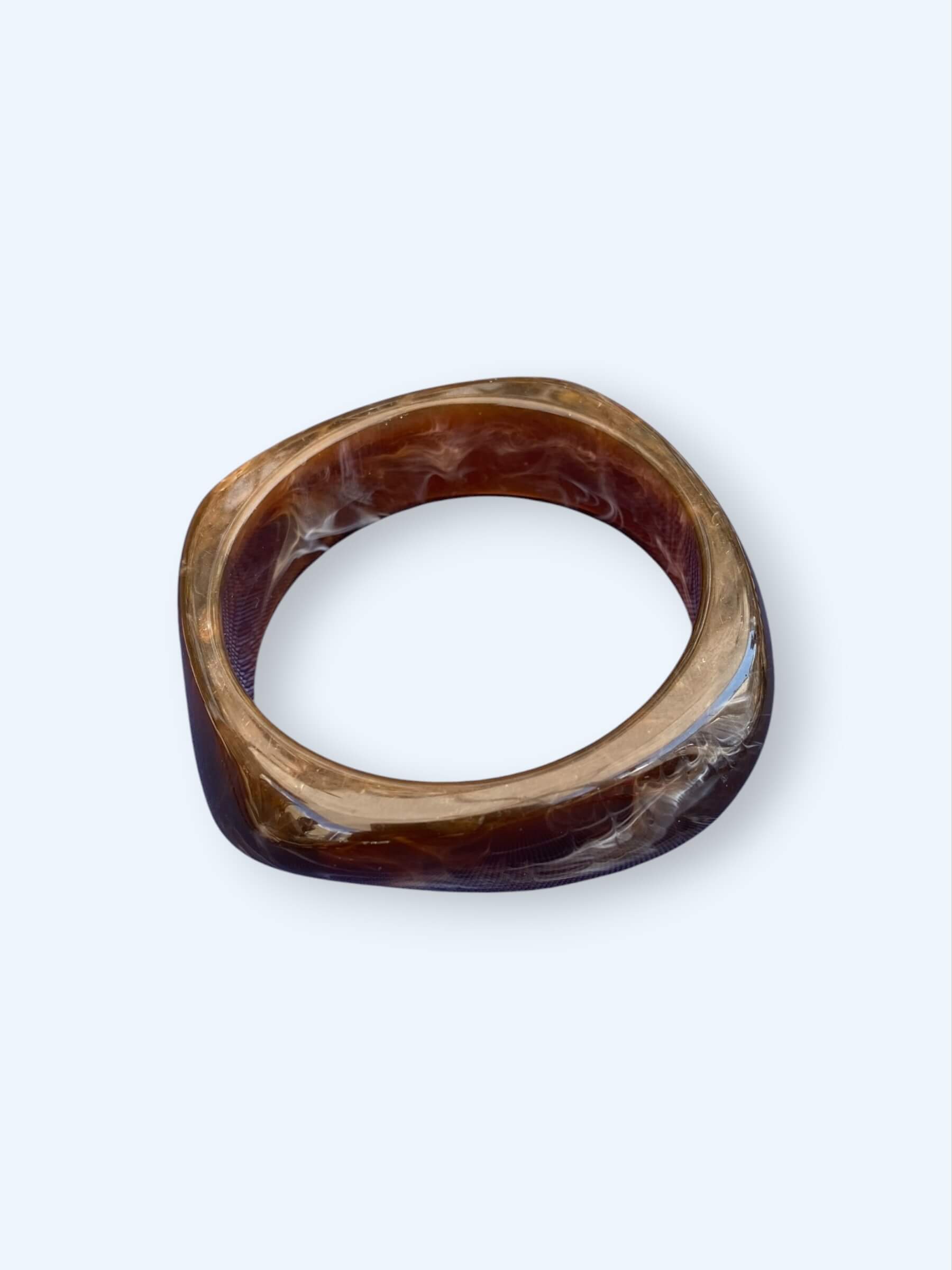 Vista da pulseira castanha que pertence ao Conjunto de três pulseiras em resina. Estas pulseiras tem acabamento glossy e são dos tons pretos e castanho, são perfeitas para combinar com tudo ou para usar sem nada. São o acessório perfeito para o verão.