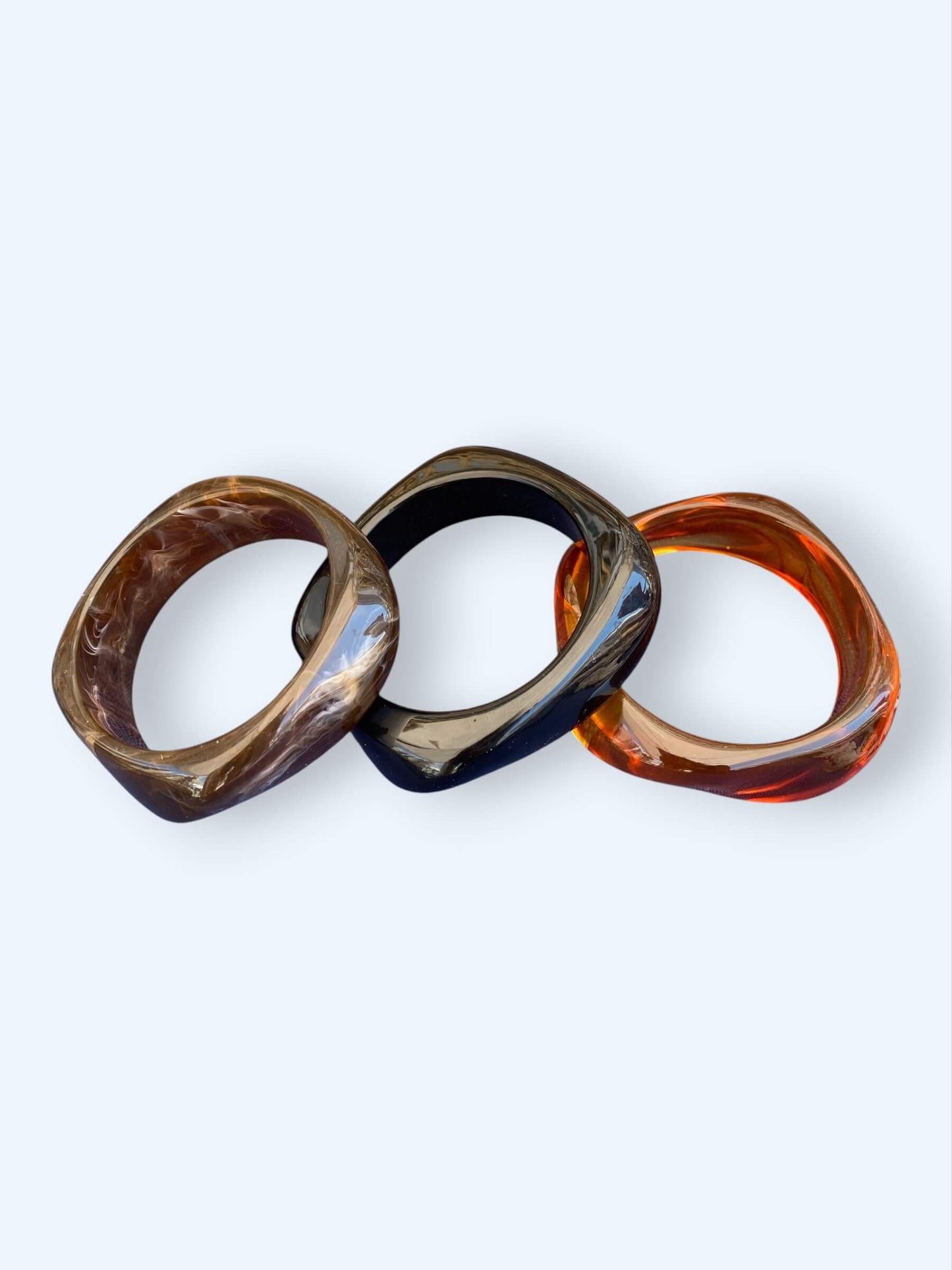 Vista conjunta do Conjunto de três pulseiras em resina. Estas pulseiras tem acabamento glossy e são dos tons pretos e castanho, são perfeitas para combinar com tudo ou para usar sem nada. São o acessório perfeito para o verão.