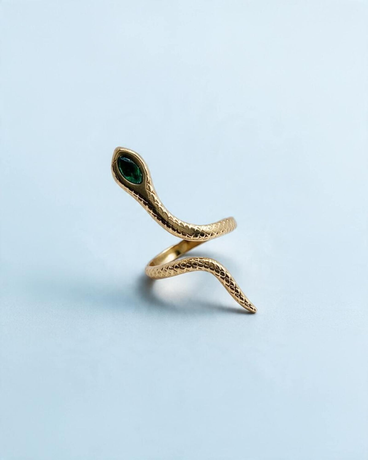 Anel Víbora dourado em aço inoxidável, em forma de serpente com textura de escamas e detalhe verde na cabeça.