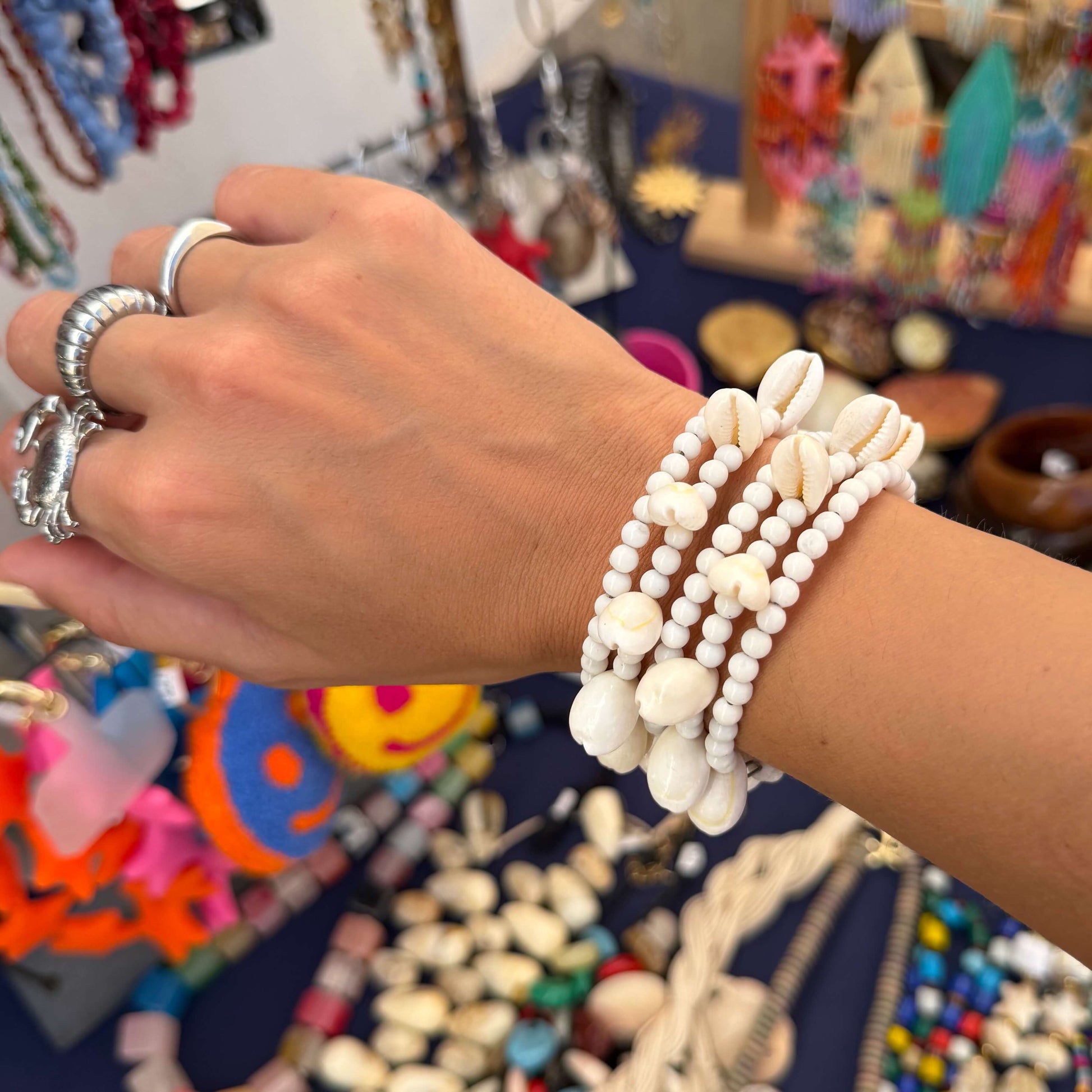 Vista superior da Pulseira ajustável com missangas brancas grandes e búzios. Pulseira leve e descontraída perfeita para looks de verão, na praia e na cidade. Pulseira ideal para festivais e festas.