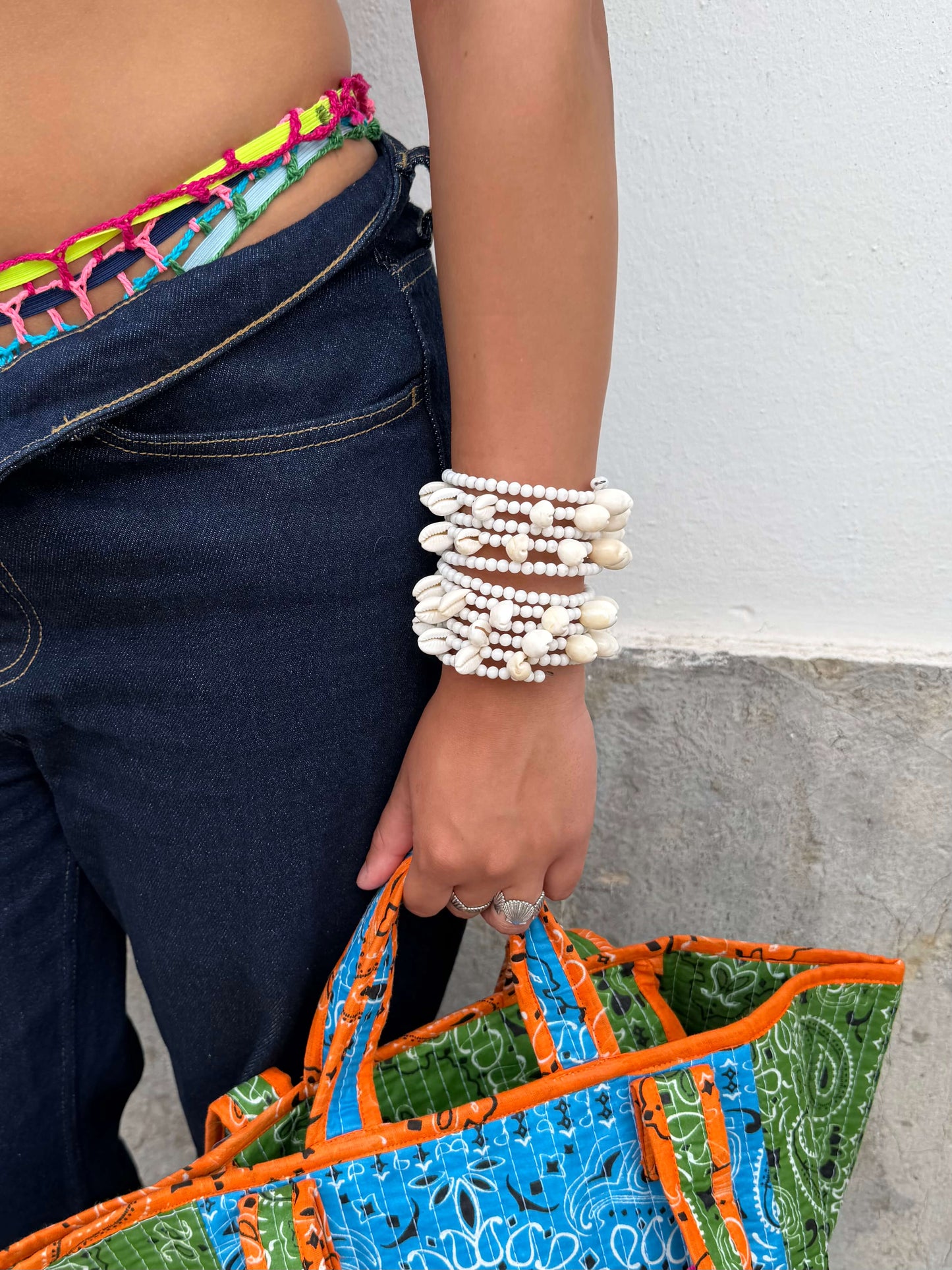 Vista superior da Pulseira ajustável com missangas brancas grandes e búzios. Pulseira leve e descontraída perfeita para looks de verão, na praia e na cidade. Pulseira ideal para festivais e festas.