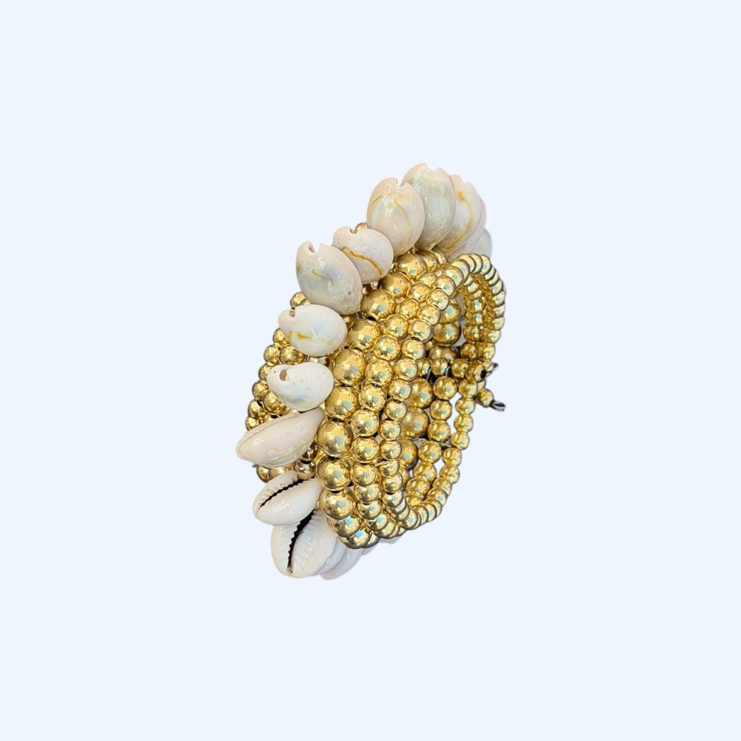 Vista lateral da Pulseira com búzios naturais e esferas douradas metálicas. Esta pulseira tem uma estética mix cool entre um tribal e boho beachy. É uma pulseira com búzios serve aos looks mais basic aos mais irreverentes.