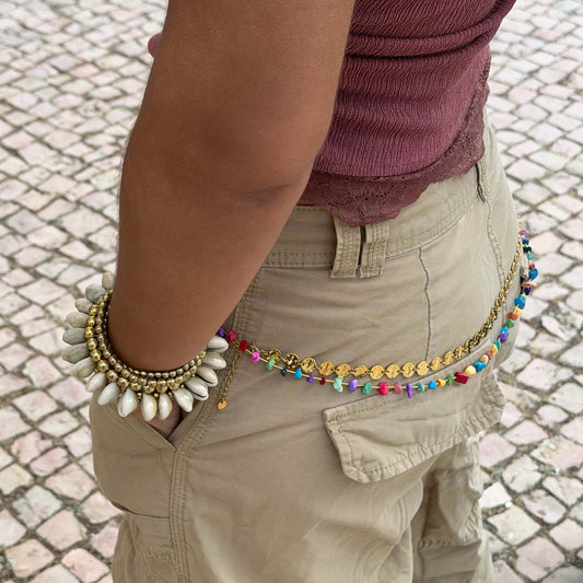Vista lateral da Pulseira com búzios naturais e esferas douradas metálicas. Esta pulseira tem uma estética mix cool entre um tribal e boho beachy. É uma pulseira com búzios serve aos looks mais basic aos mais irreverentes.