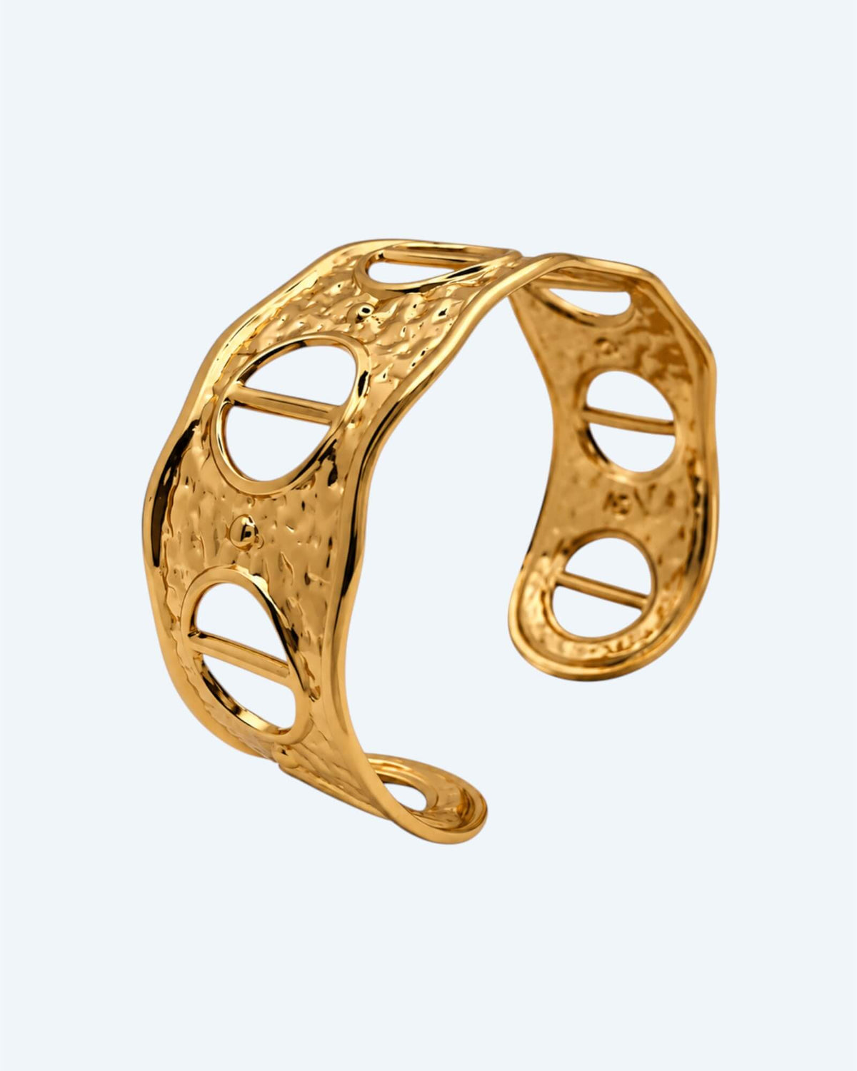 Vista na diagonal da Pulseira dourada rígida, ajustável, em aço inoxidável, martelada com aberturas. Esta pulseira é uma versão contemporânea de boho vintage. É para quem gosta de looks marcantes ou para quem procura uma pulseira para usar numa ocasião especial ou cerimónia.
