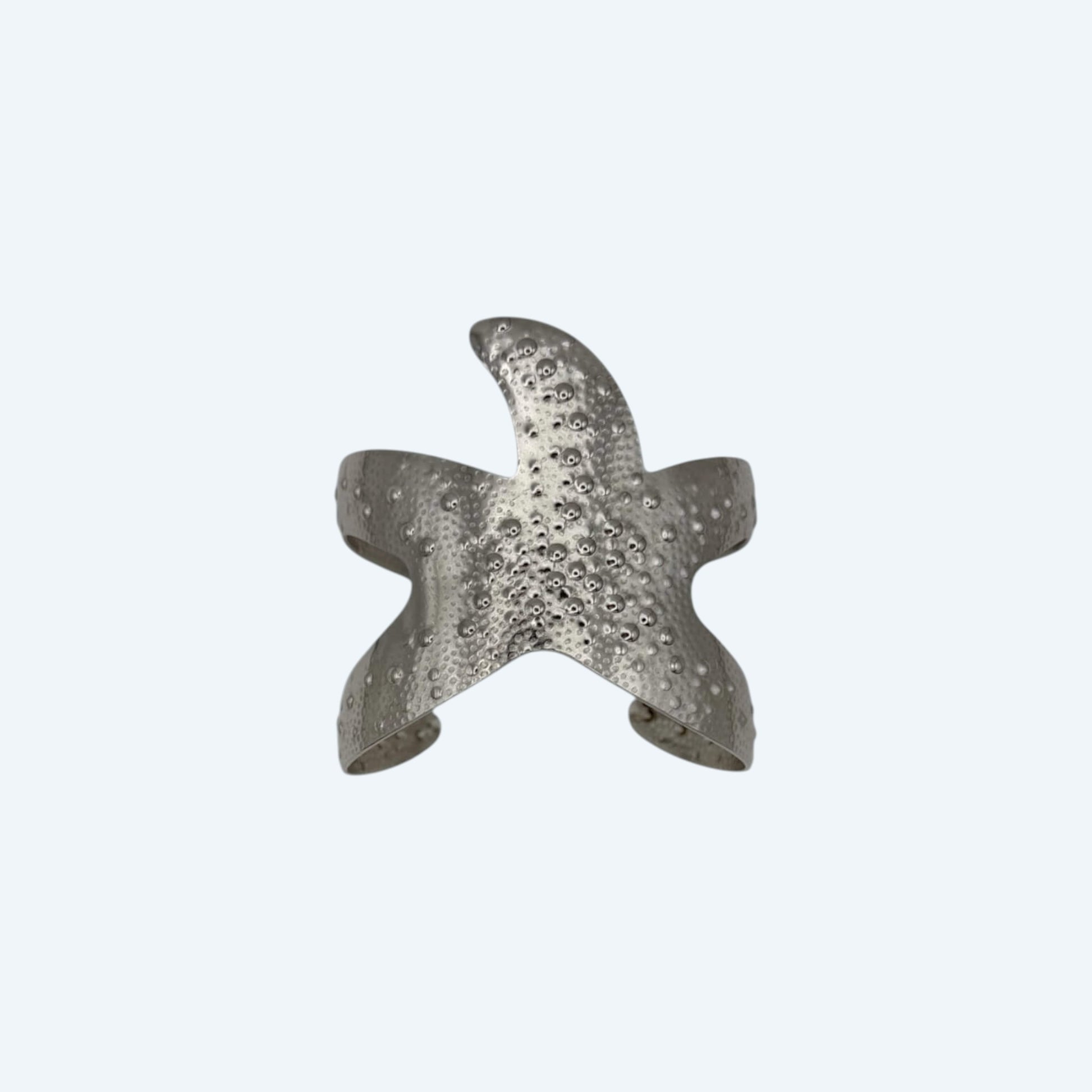 Vista frontal da pulseira larga prateada, com formato de estrela do mar grande, em aço inoxidável de bracelete ajustável. Pulseira de verão com beach energy para looks de verão, looks de festas, sunsets, festivais ou para o dia a dia.
