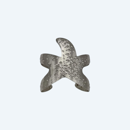 Vista frontal da pulseira larga prateada, com formato de estrela do mar grande, em aço inoxidável de bracelete ajustável. Pulseira de verão com beach energy para looks de verão, looks de festas, sunsets, festivais ou para o dia a dia.